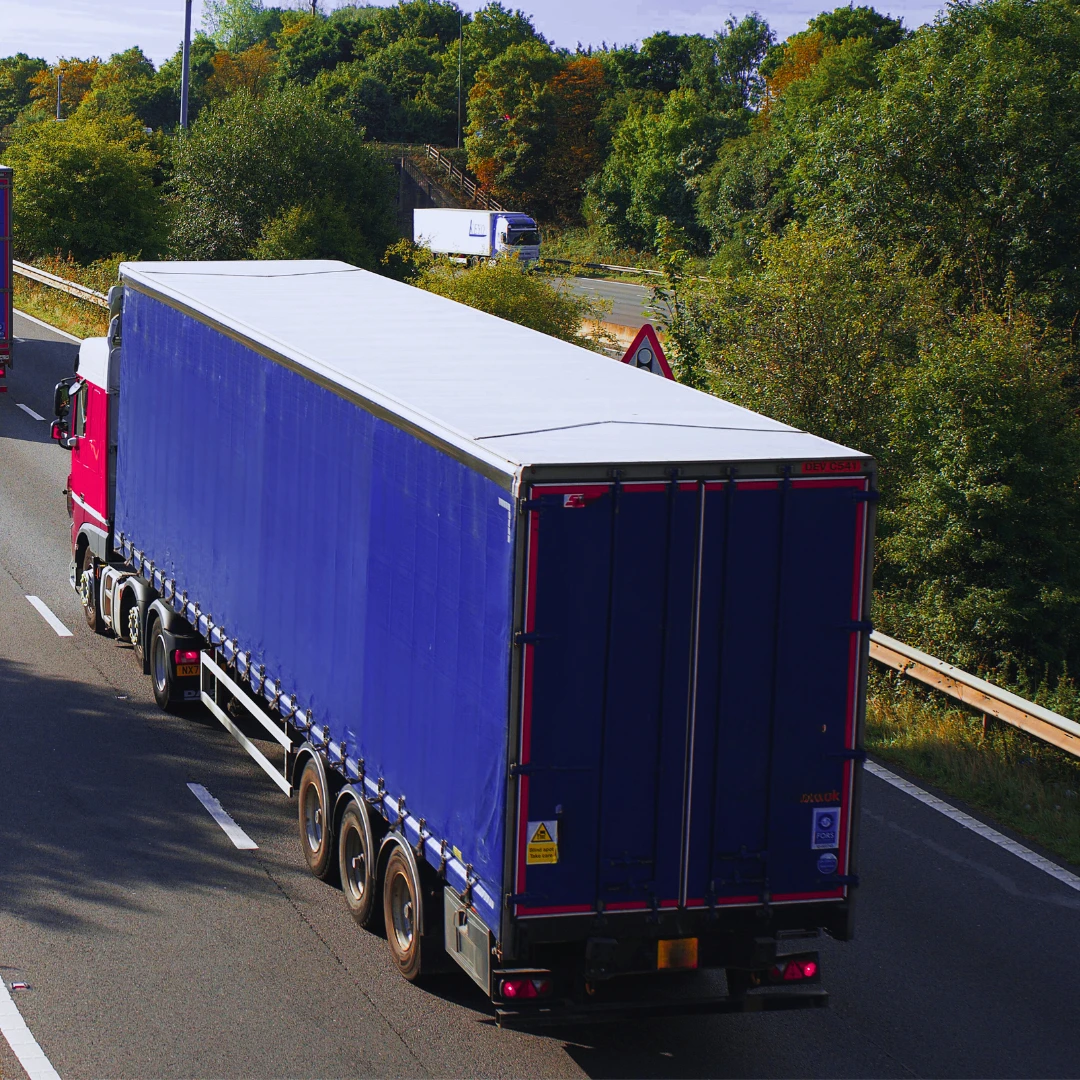 Rear view of an articulated lorry with a blue curtain-side trailer driving on a dual carriageway