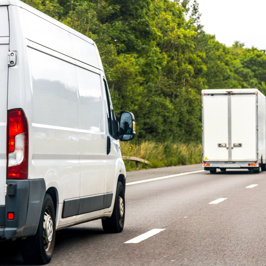White vans driving on a two-lane road with greenery in the background
