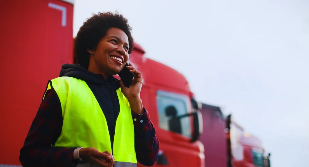 Smiling fleet manager in high-vis vest speaking on phone with red ex Royal Mail trucks in background