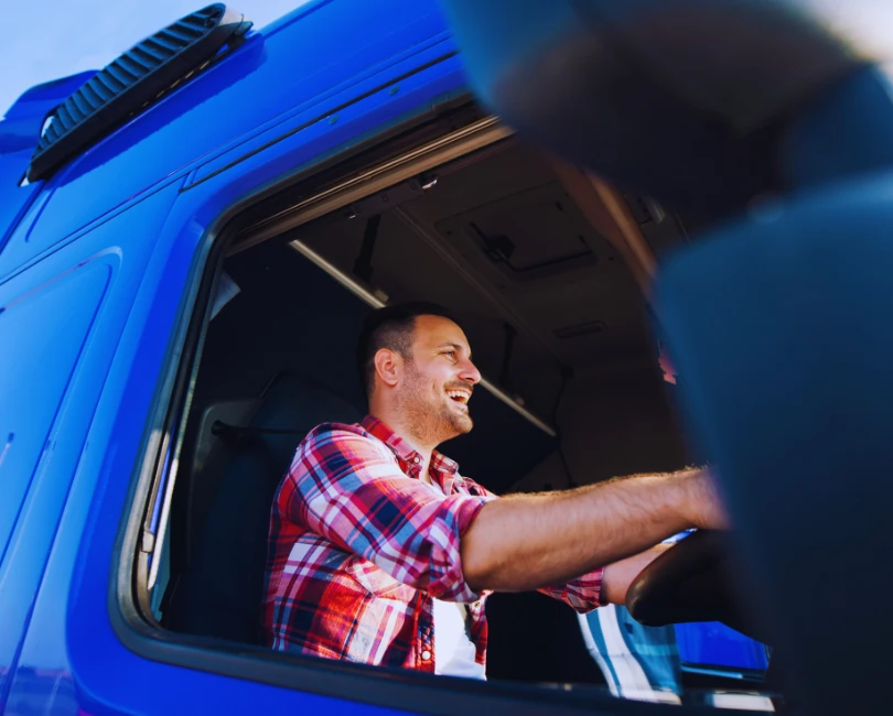 Smiling HGV driver wearing a checked shirt inside a blue truck cab