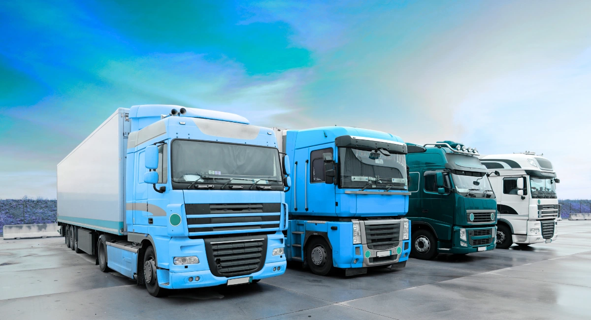 Line of mixed fleet vehicles including box trucks and articulated HGVs on a depot lot, suitable for fleet CCTV system