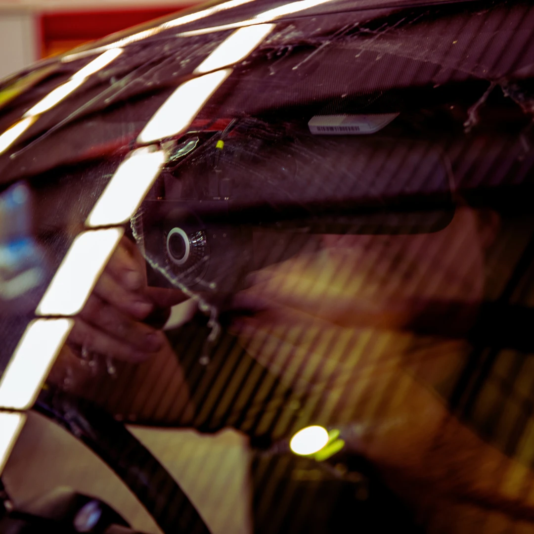 Close-up view of a technician installing a dash cam inside a vehicle, seen through the windscreen